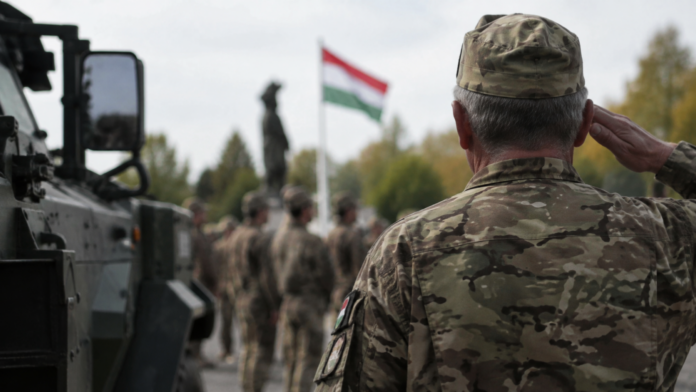 katona Idősebb magyar katona tiszteleg egy katonai alakulat előtt, háttérben magyar zászlóval és katonai járművel.