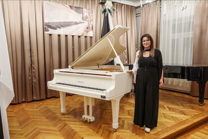 zenevilágnapja (78) Nyitott fedelű fehér Yamaha zongora és mellette álló nő a kiskőrösi SZÓ-LA-M művészeti iskola hangversenytermében.